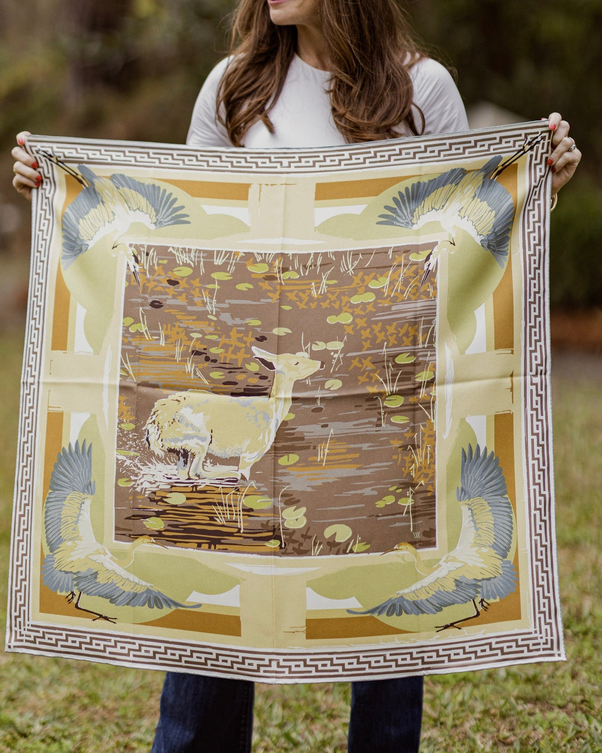 Person holding a large decorative scarf with a nature-themed design outdoors.