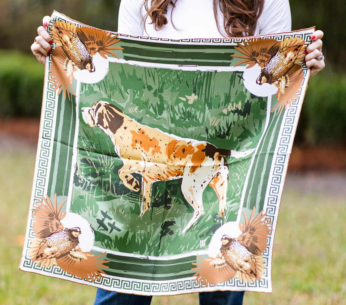 Person holding a green scarf with a dog and bird design.